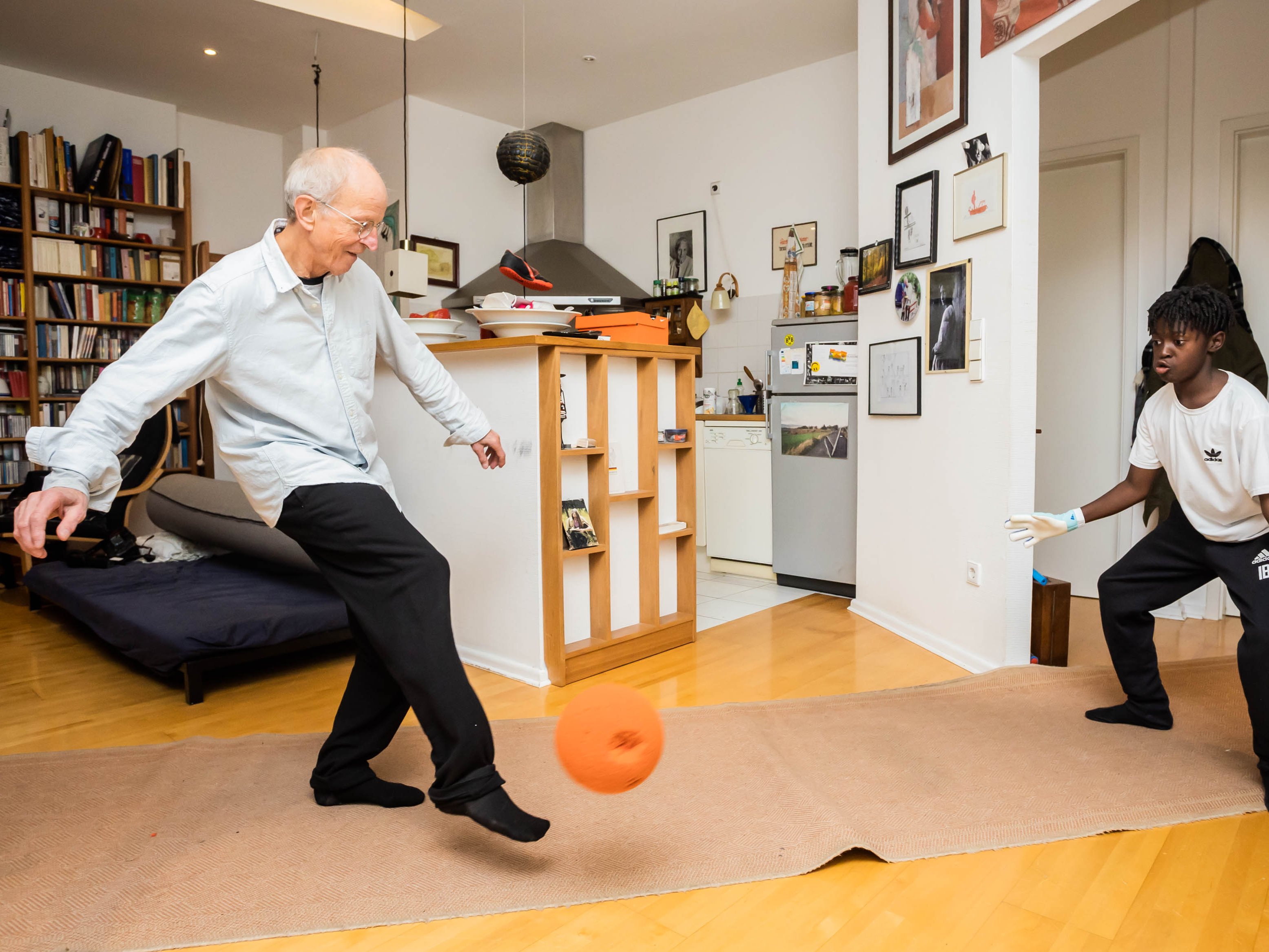 Ein älterer Mann spielt mit einem Kind Fußball in der Wohnung.