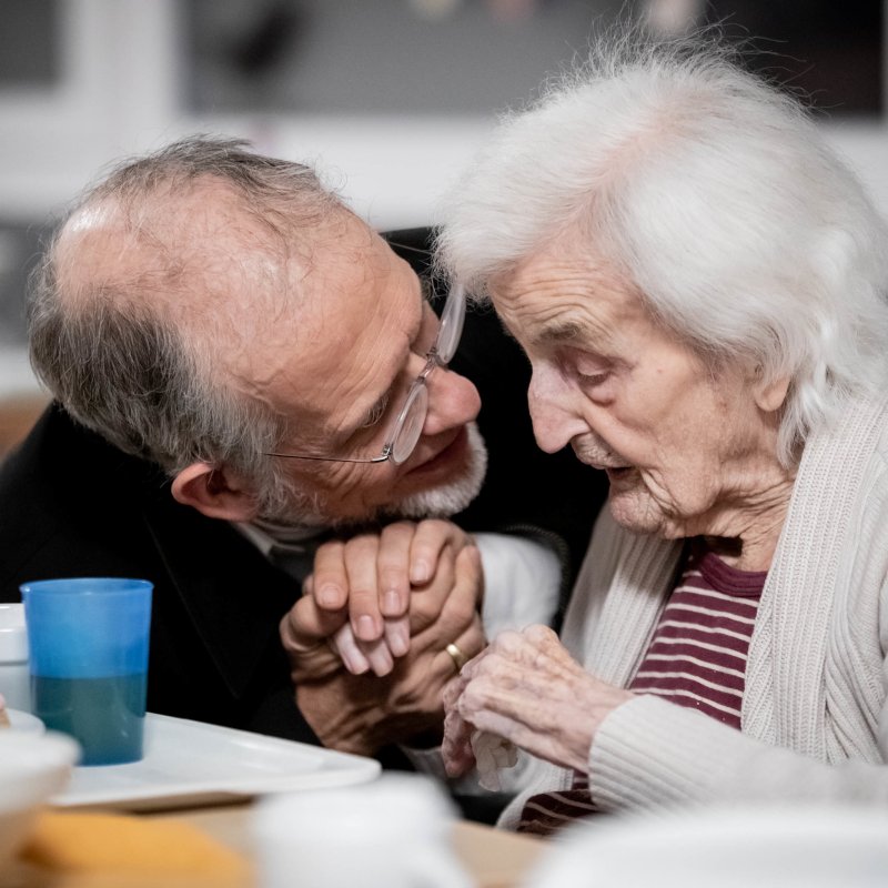 Älterer Mann und Seniorin, älterer Mann hält die Hand der Seniorin und schaut ihr bestärkend ins Gesicht.